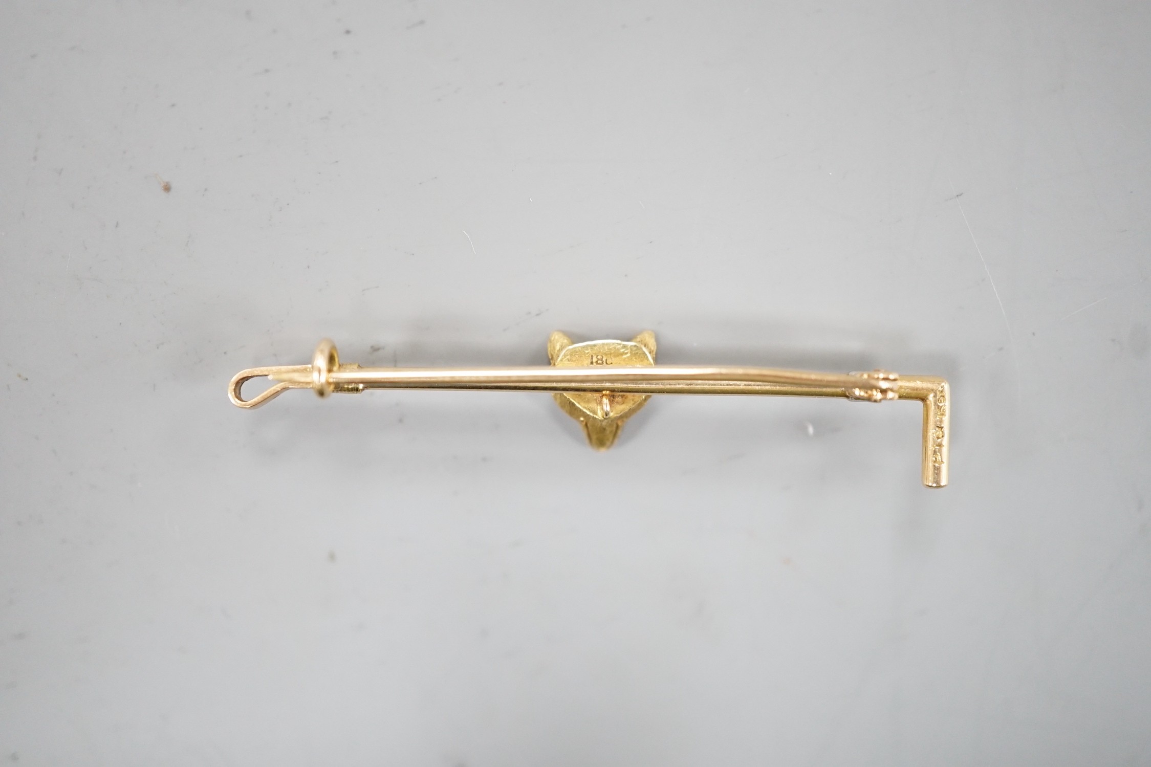 An 18ct and gem set fox head and riding crop bar brooch, 50mm, gross weight 4 grams.